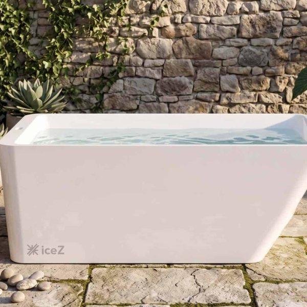 Modern white acrylic ice bath outdoors with plants and stone wall.